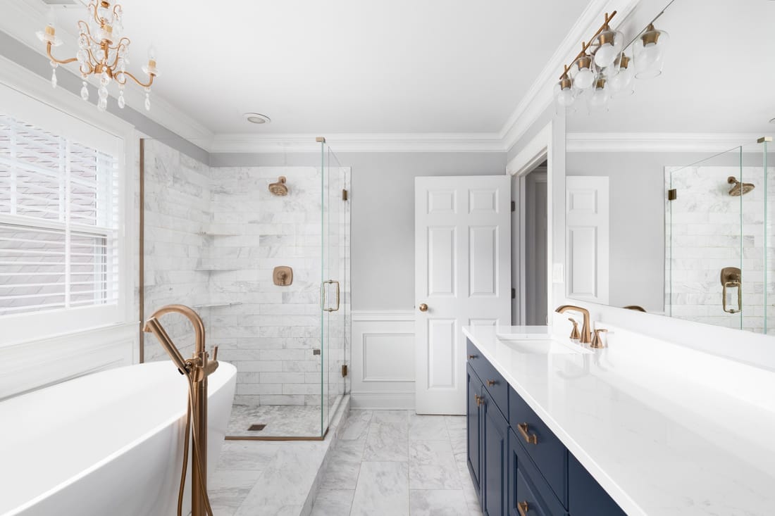 Marble bathroom remodel in Sacramento — navy vanity, brass fixtures, freestanding tub, and glass shower