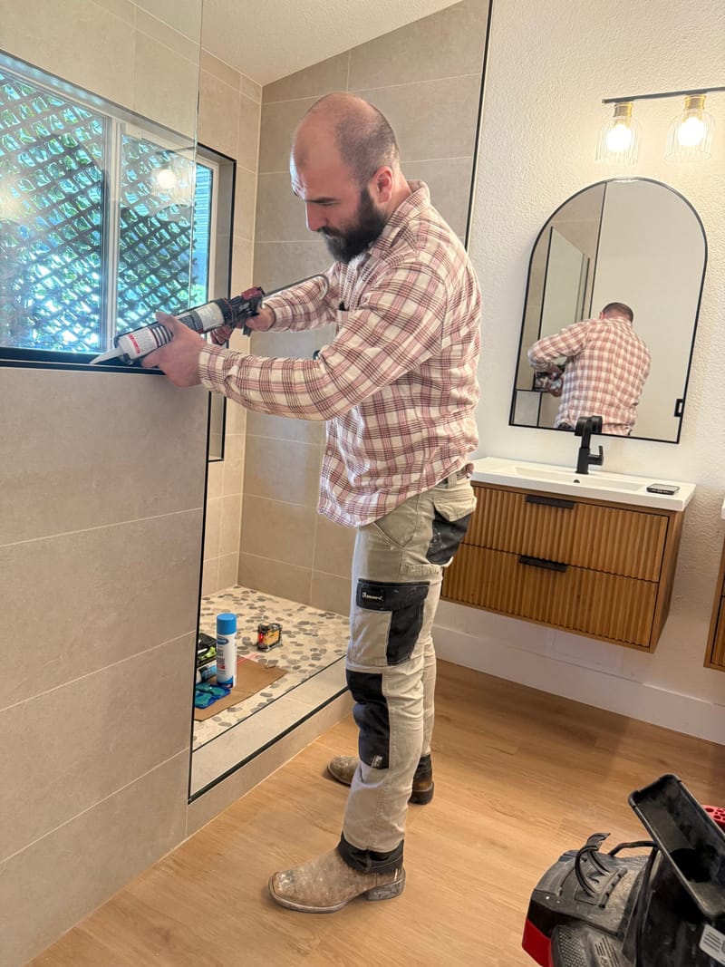 Stonebrite owner Abel Vaniyev sealing a shower glass panel on a finished bathroom remodel