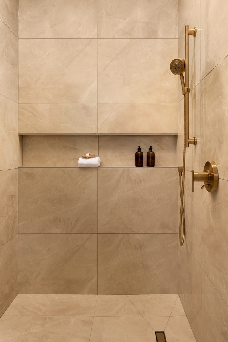 Tiled shower with brass fixtures, recessed niche, and linear drain